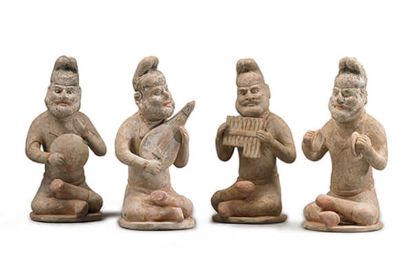 唐代．加彩胡人樂俑+四位胡人雙腿交疊盤坐在小圓氈上，手上拿著各式樂器，神情愉悅地演奏音樂。（圖三）